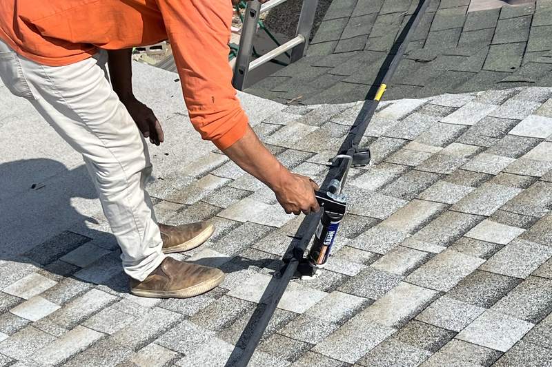 Worker handling roof-mounted rail hardware over asphalt shingles