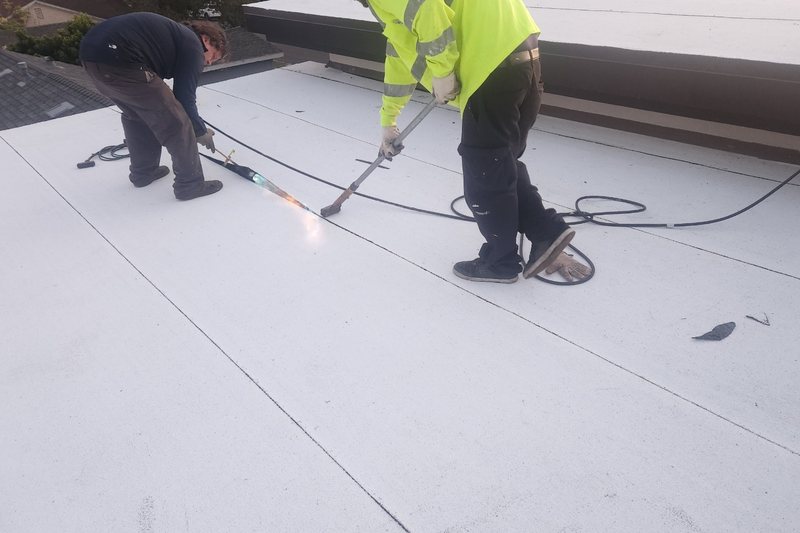 Two workers performing close low-slope roofing work