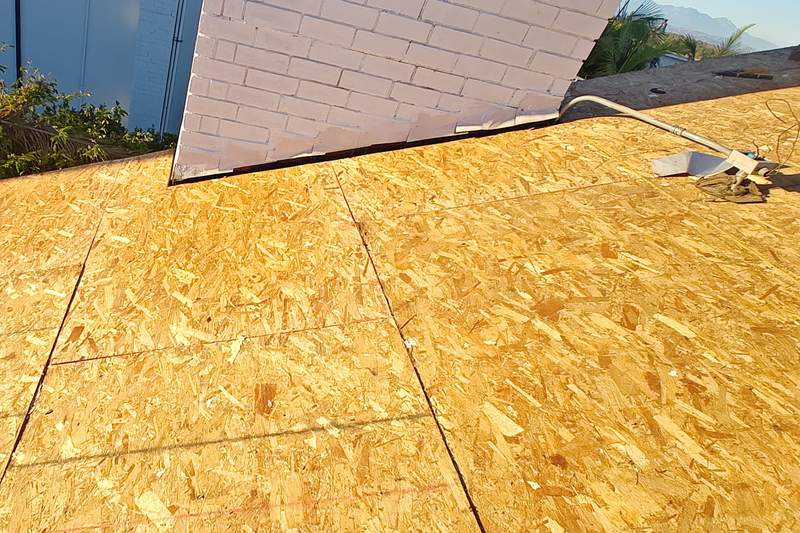 OSB roof sheathing beside a masonry chimney during installation work