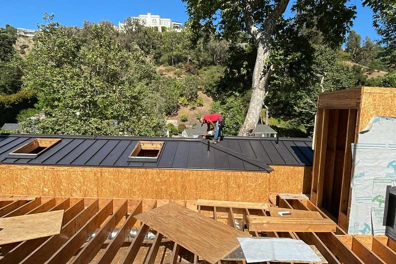 Roofers working across new framing, sheathing, and metal roof sections