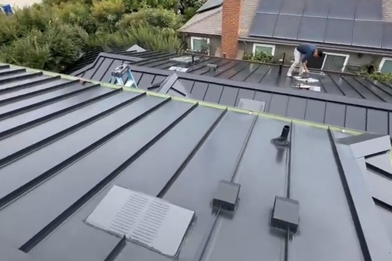 Dark standing-seam metal roof planes with raised seams and low-profile components