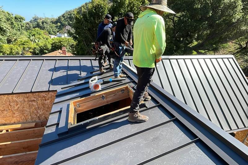 Roofers working around standing-seam metal panels and an open roof section