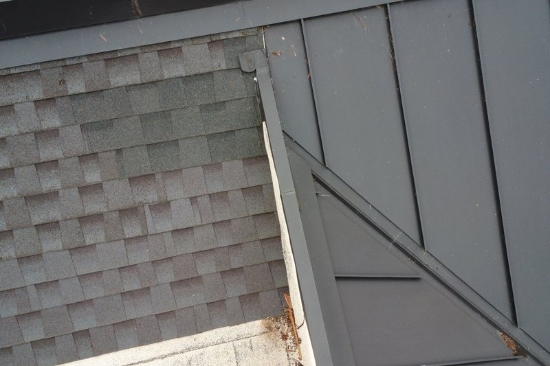 Asphalt shingles meeting a dark metal-clad wall