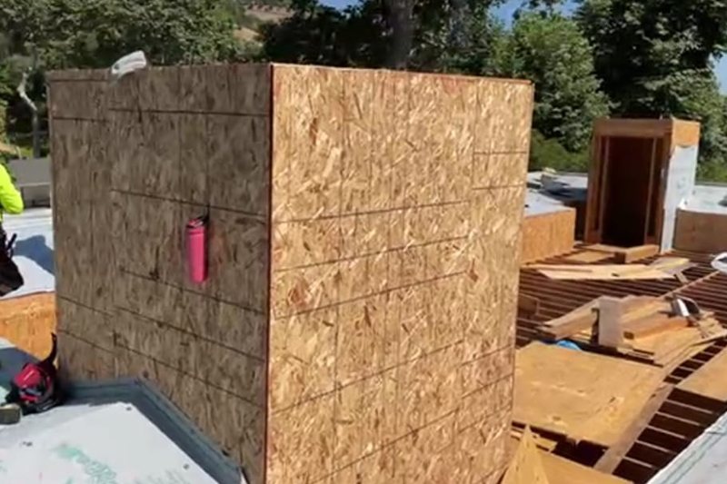 OSB-sheathed chimney chase beside open roof framing during construction