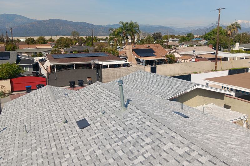 Light-gray shingle roof above a low-rise neighborhood with distant hills
