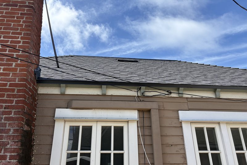 Shingle roof edge with fascia, gutter, and a masonry chimney above a wood-sided wall